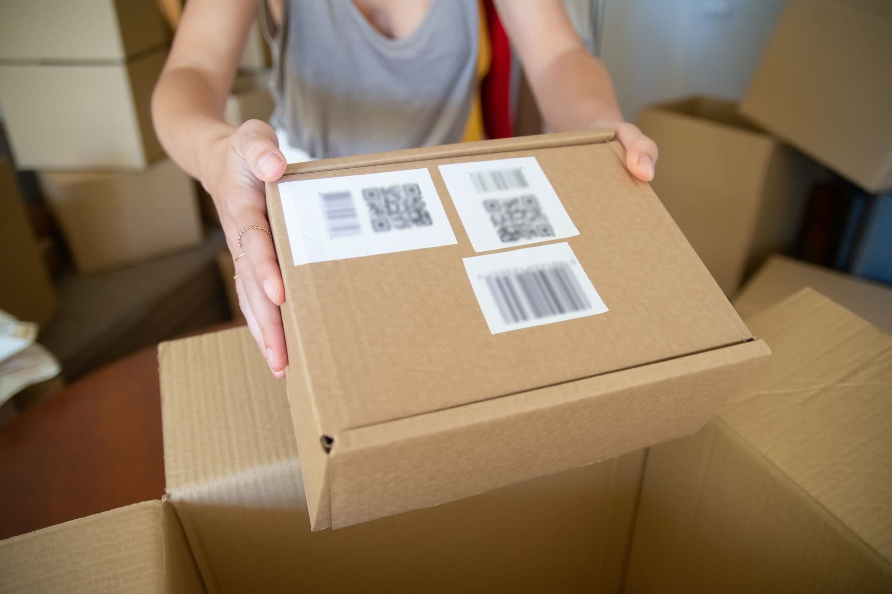 Hands holding a cardboard box with barcode labels on the lid