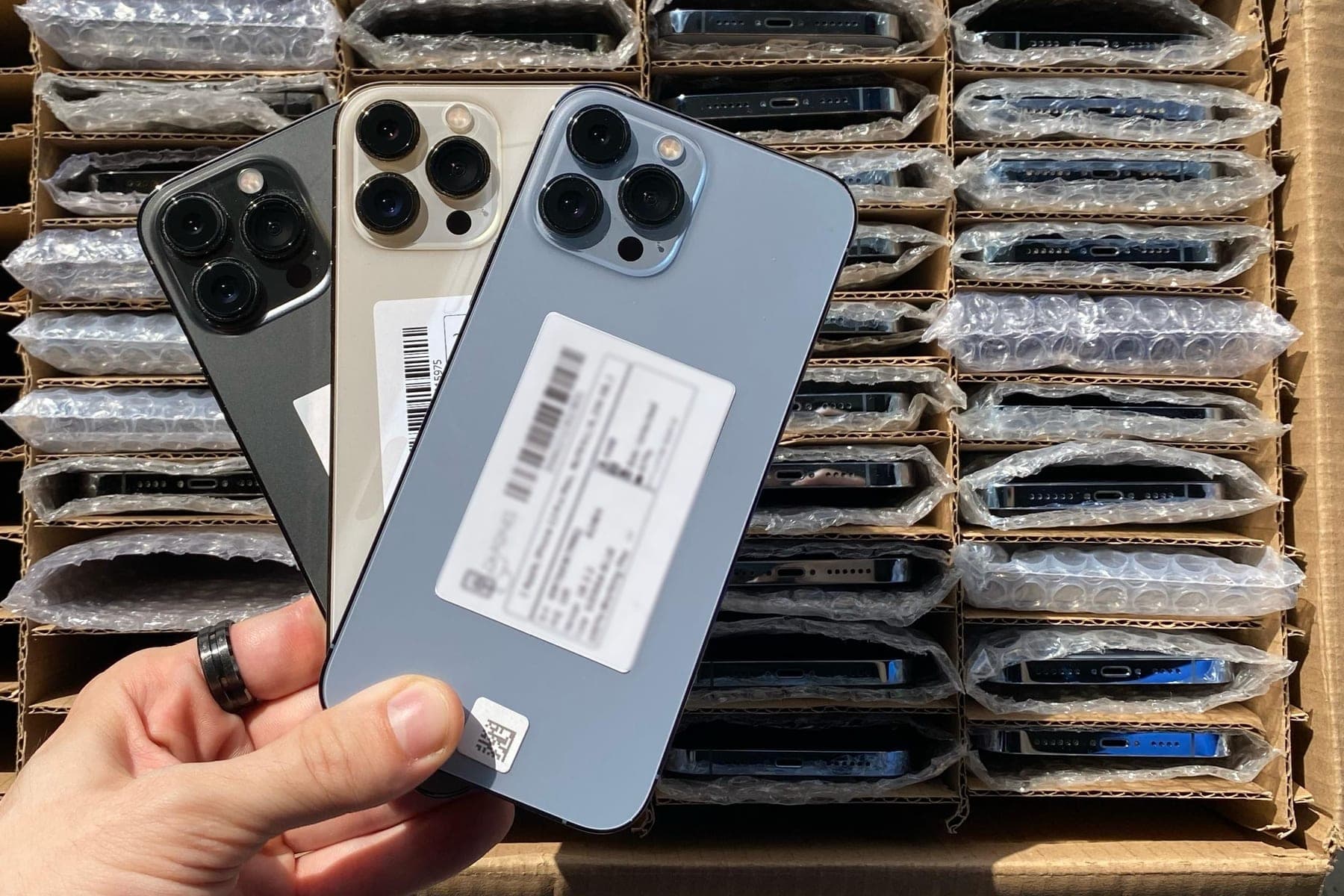 A hand holding three used devices over a carton of more, each wrapped in bubble wrap
