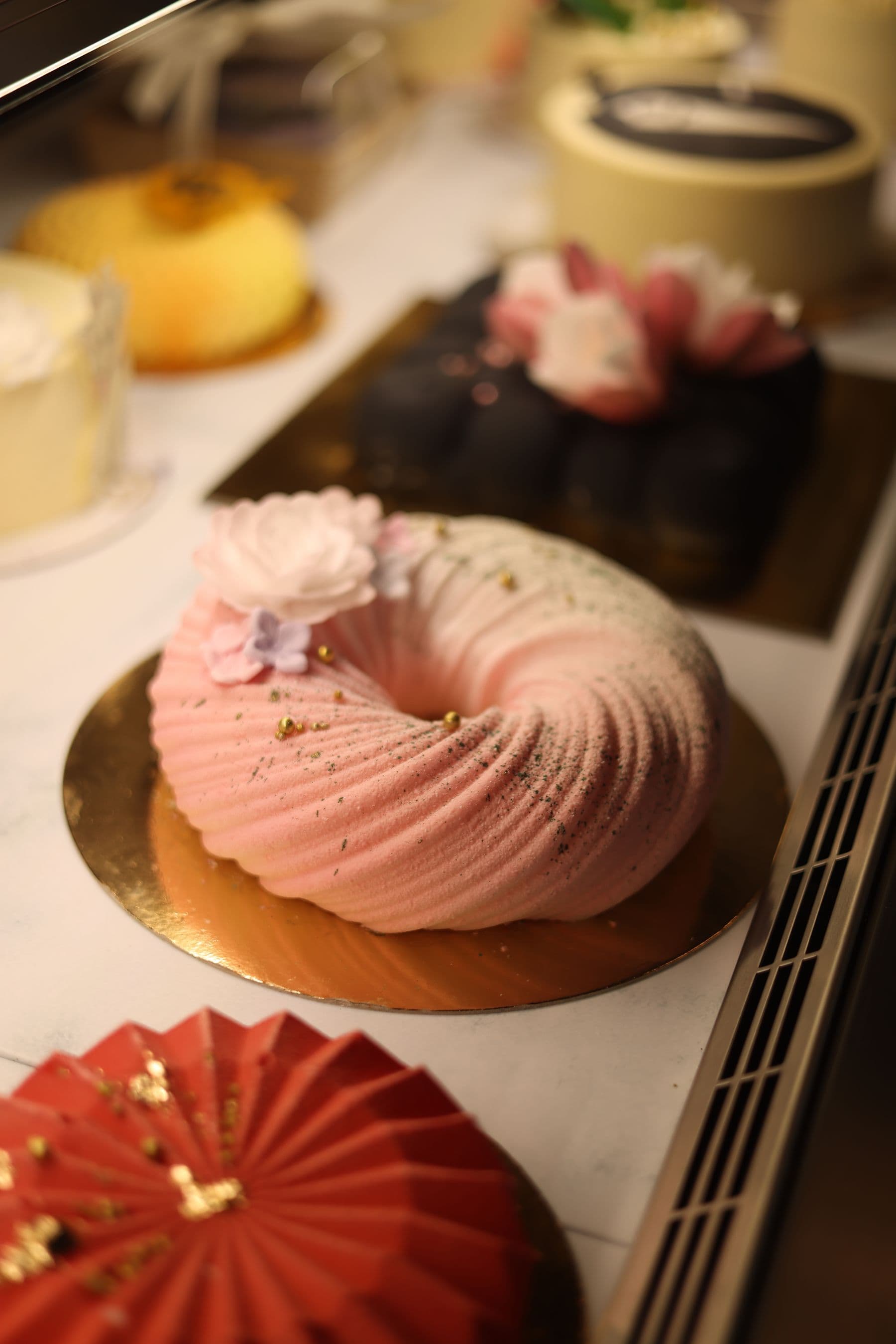 A pink cake with sugar flowers in a bakery case
