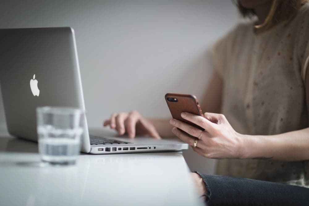 Someone scrolling on a phone next to a laptop