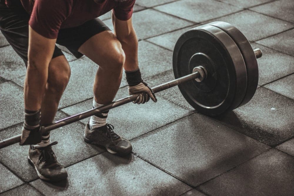 A lifter gripping a loaded barbell on a gym floor